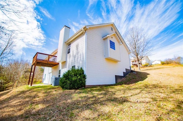 view of side of property with a yard, central AC unit, a chimney, and a deck