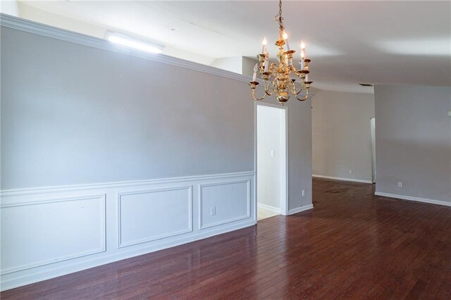 spare room featuring a notable chandelier, crown molding, and dark wood-type flooring