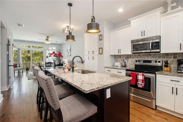 kitchen featuring stainless steel appliances, white cabinetry, decorative light fixtures, and a kitchen island with sink