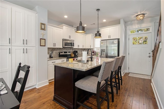 kitchen with sink, stainless steel appliances, a center island with sink, hardwood / wood-style floors, and decorative light fixtures