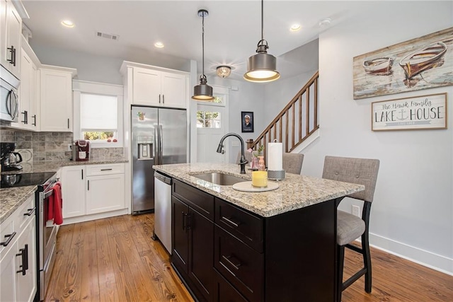 kitchen with light wood-type flooring, sink, an island with sink, a kitchen bar, and stainless steel appliances