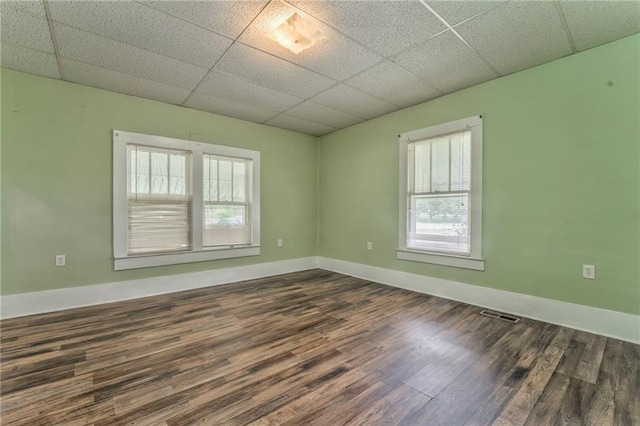 empty room with healthy amount of natural light, wood finished floors, a paneled ceiling, and baseboards