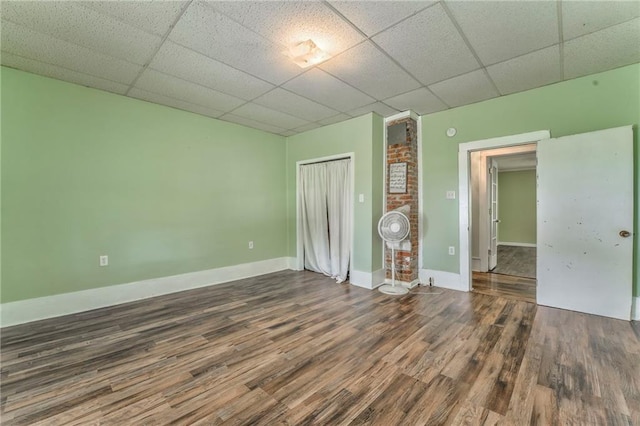 unfurnished bedroom featuring a drop ceiling, wood finished floors, a closet, and baseboards