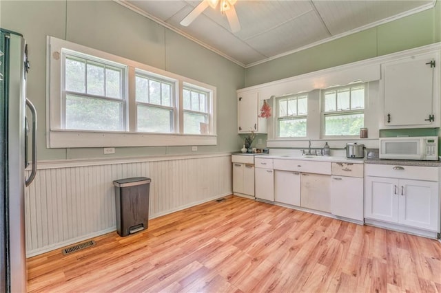 kitchen with white microwave, light wood-type flooring, crown molding, freestanding refrigerator, and white cabinetry