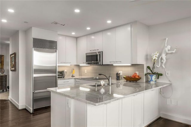 kitchen with appliances with stainless steel finishes, baseboards, a peninsula, and dark wood-style floors