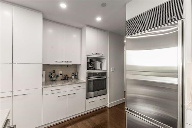 kitchen with decorative backsplash, recessed lighting, white cabinetry, dark wood finished floors, and appliances with stainless steel finishes