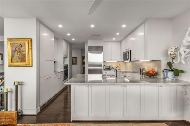 kitchen featuring backsplash, white cabinets, black appliances, a peninsula, and recessed lighting