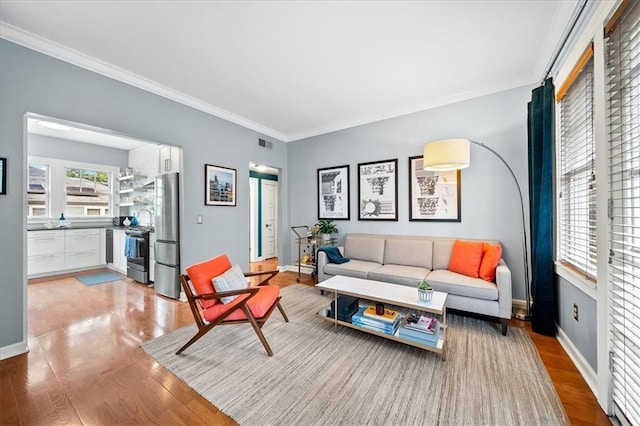 living area with visible vents, baseboards, light wood-style flooring, and ornamental molding