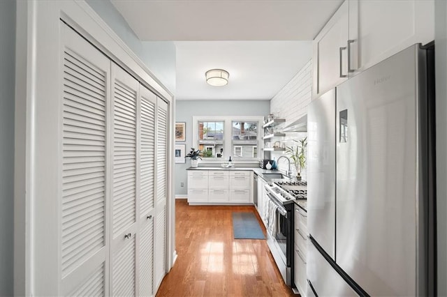 kitchen with light wood-type flooring, a sink, open shelves, stainless steel appliances, and white cabinets