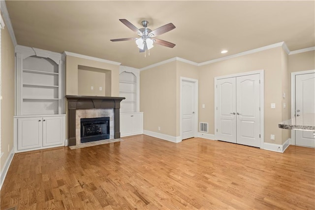 unfurnished living room featuring built in shelves, a tile fireplace, ornamental molding, and light hardwood / wood-style flooring