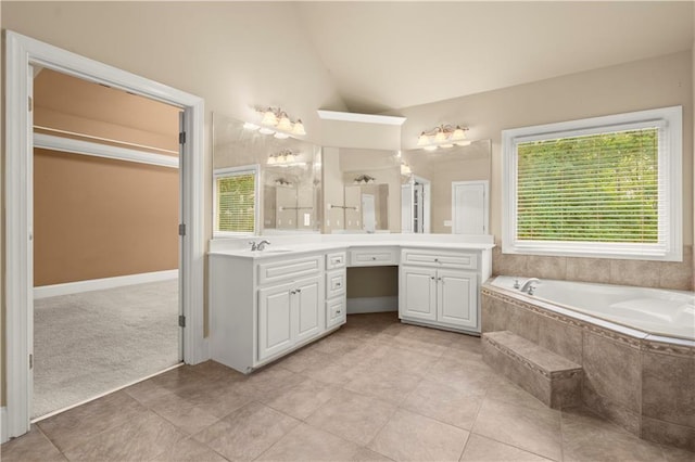 bathroom featuring vaulted ceiling, a healthy amount of sunlight, tiled tub, and vanity