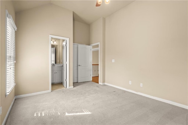 unfurnished bedroom featuring ensuite bath, light carpet, and lofted ceiling