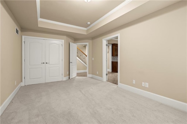 unfurnished bedroom featuring a tray ceiling, a closet, crown molding, and light carpet