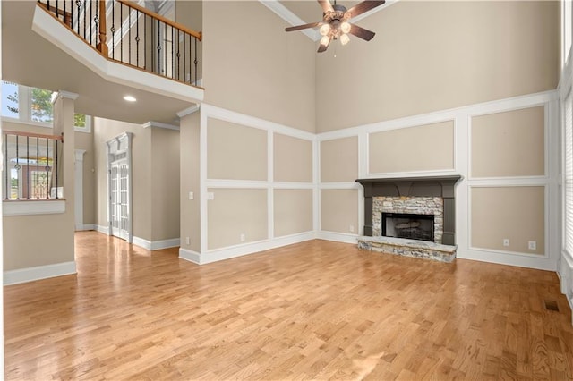 unfurnished living room with ceiling fan, light hardwood / wood-style flooring, a stone fireplace, and a towering ceiling