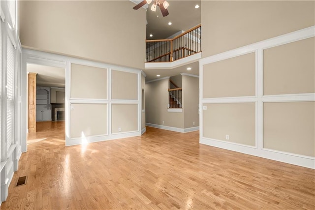 unfurnished living room featuring ceiling fan, a high ceiling, crown molding, and light hardwood / wood-style floors