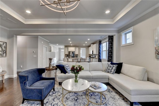 living area featuring baseboards, a chandelier, ornamental molding, wood finished floors, and a raised ceiling