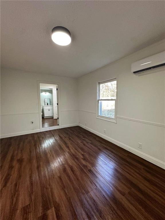 spare room with a textured ceiling, a wall unit AC, and dark hardwood / wood-style floors