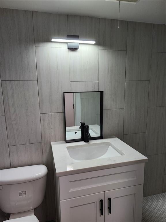 bathroom featuring toilet, tile walls, and vanity