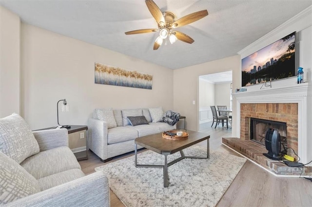 living room with light hardwood / wood-style floors, a brick fireplace, ceiling fan, and crown molding