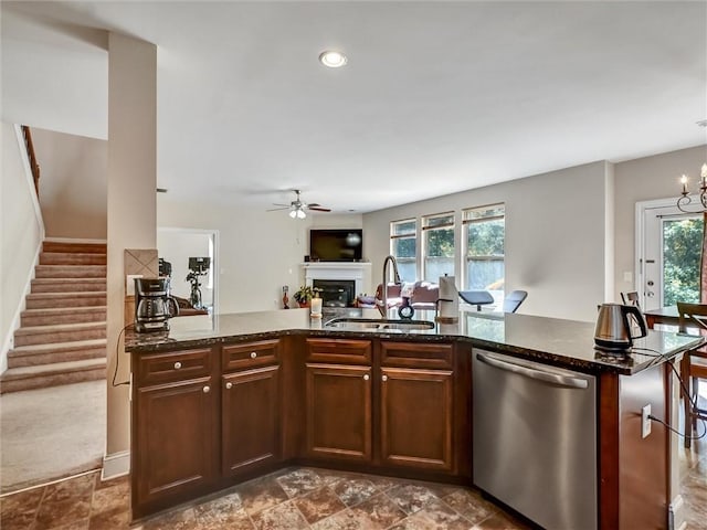 kitchen with stainless steel dishwasher, a sink, open floor plan, ceiling fan with notable chandelier, and a fireplace