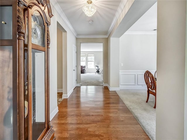 hall with a wainscoted wall, baseboards, an inviting chandelier, wood finished floors, and crown molding
