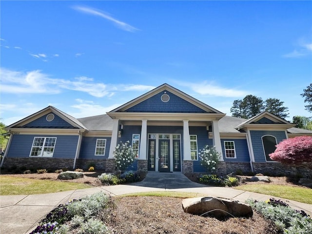 view of front of home with stone siding, a porch, and french doors