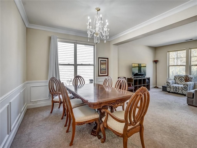 dining room with wainscoting, light carpet, an inviting chandelier, and crown molding
