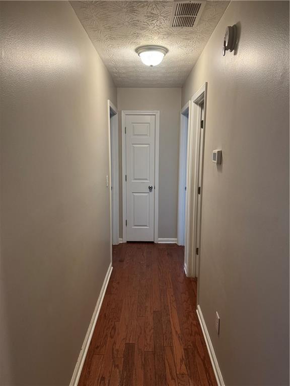 hallway featuring visible vents, a textured ceiling, dark wood-type flooring, and baseboards