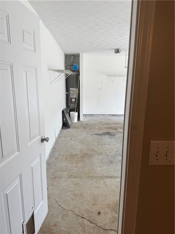 hall featuring water heater, visible vents, a textured ceiling, and unfinished concrete flooring