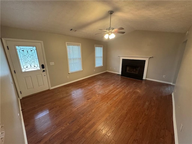 unfurnished living room featuring a ceiling fan, lofted ceiling, a fireplace with flush hearth, dark wood-type flooring, and a textured ceiling