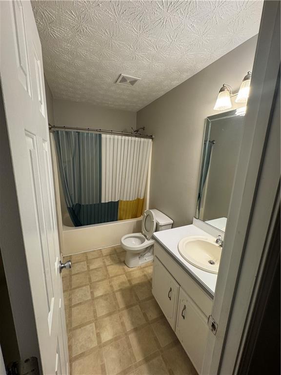 bathroom featuring visible vents, toilet, shower / bath combo with shower curtain, tile patterned floors, and vanity