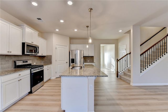 kitchen featuring a sink, white cabinets, appliances with stainless steel finishes, light wood-type flooring, and a center island with sink