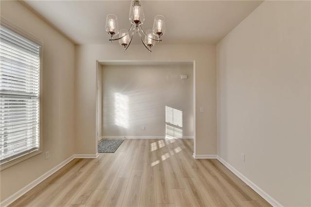 unfurnished dining area featuring baseboards, light wood-style floors, and a notable chandelier