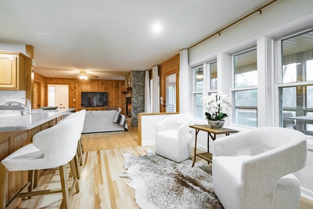 living room with light hardwood / wood-style flooring, ceiling fan, wooden walls, and sink