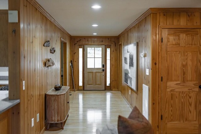 entryway with ornamental molding and wooden walls