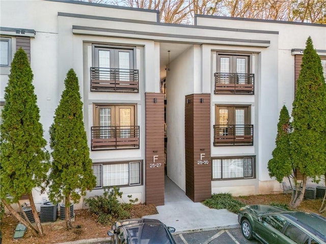 view of front of home featuring french doors, a balcony, uncovered parking, and stucco siding