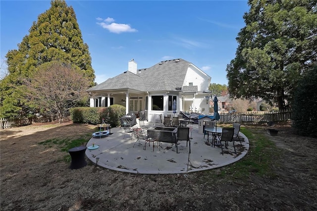 rear view of property featuring a patio area, a chimney, an outdoor fire pit, and fence