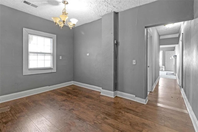 unfurnished dining area with an inviting chandelier, a textured ceiling, and dark hardwood / wood-style flooring