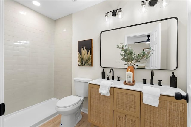 bathroom featuring wood-type flooring, vanity, a tile shower, and toilet