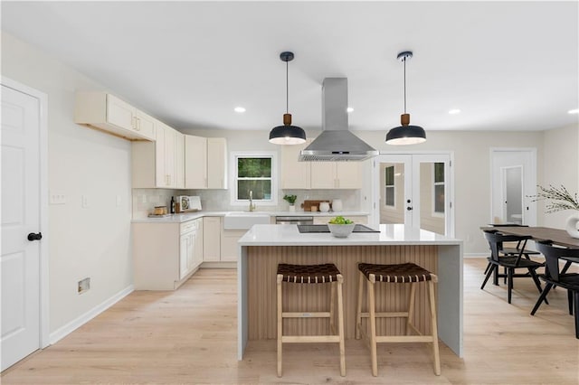 kitchen featuring sink, light hardwood / wood-style flooring, decorative backsplash, a kitchen island, and island range hood