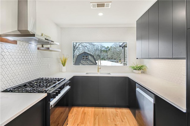 kitchen featuring wall chimney range hood, sink, light hardwood / wood-style flooring, dishwasher, and gas stove