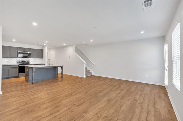 323 Rolling Green Rd, Adairsville, GA 30103 - kitchen featuring appliances with stainless steel finishes, gray cabinetry, decorative backsplash, light wood-style floors, and a kitchen bar