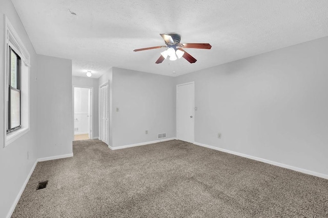 spare room with a textured ceiling, carpet floors, ceiling fan, and baseboards
