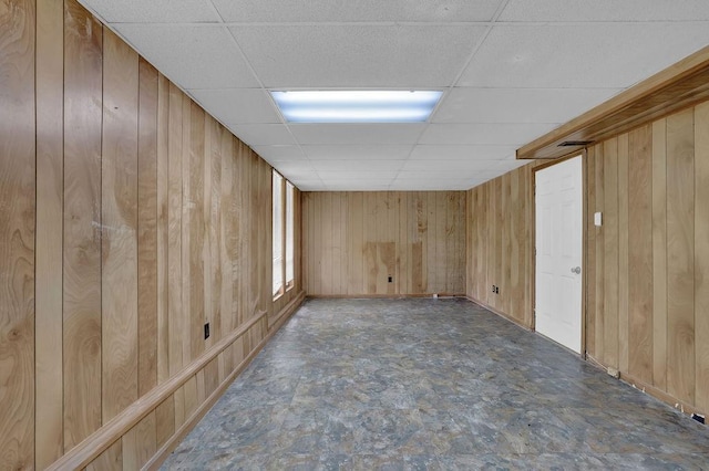 unfurnished room with a drop ceiling, wooden walls, and baseboards