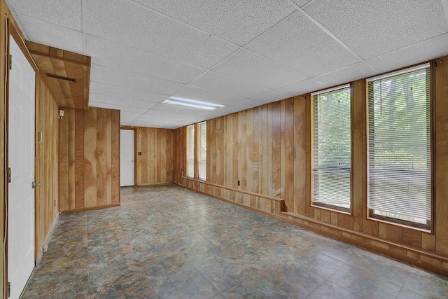 unfurnished room with wooden walls, a paneled ceiling, healthy amount of natural light, and baseboards