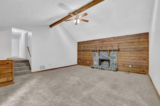 unfurnished living room with a ceiling fan, wood walls, carpet, a fireplace, and a textured ceiling