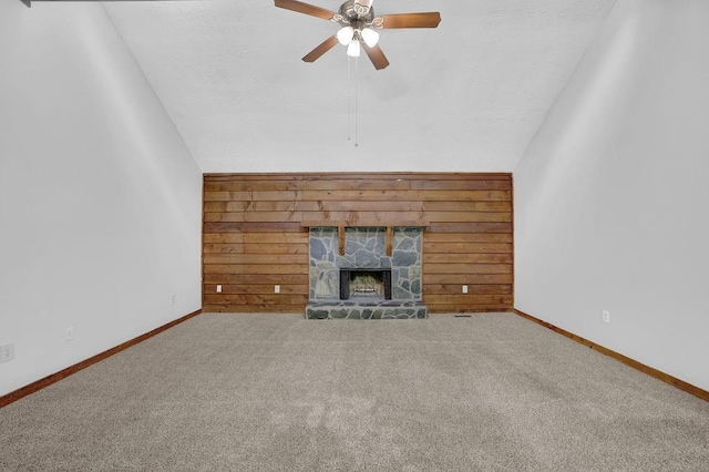 unfurnished living room featuring a ceiling fan, vaulted ceiling, wooden walls, carpet flooring, and a stone fireplace