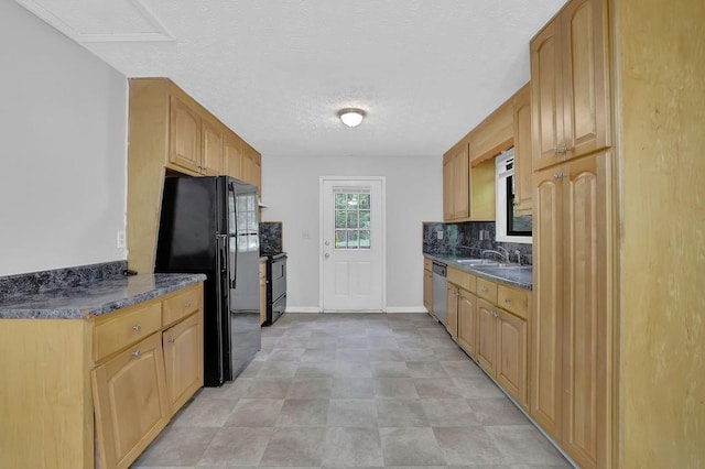 kitchen featuring freestanding refrigerator, dark countertops, stainless steel dishwasher, a sink, and decorative backsplash