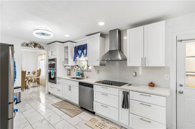 kitchen featuring marble finish floor, a sink, wall chimney range hood, stainless steel appliances, and light countertops