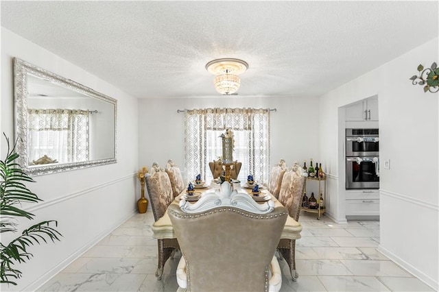 dining area featuring an inviting chandelier, baseboards, marble finish floor, and a textured ceiling